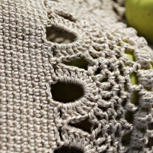 May include: Close-up of a crocheted doily with a delicate pattern and a light beige color.