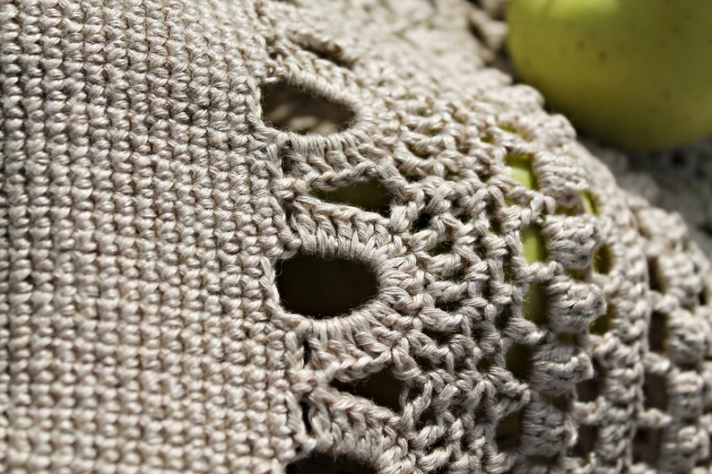 May include: Close-up of a crocheted doily with a delicate pattern and a light beige color.