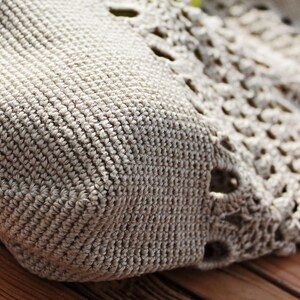 May include: Close-up of a beige crocheted bag with a textured pattern. The bag has a square shape and a crocheted design with openwork details.