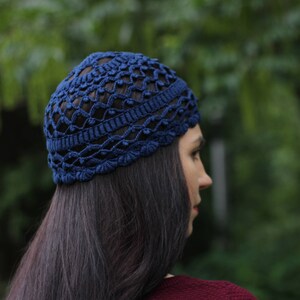 May include: A blue crocheted hat with a lacy design. The hat is worn on the head of a person with long dark hair.