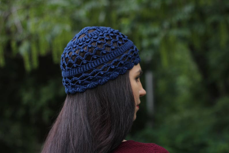 May include: A blue crocheted hat with a lacy design. The hat is worn on the head of a person with long dark hair.