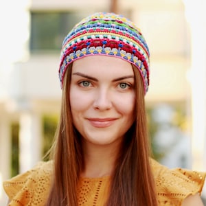 The woman wears a crocheted hat made from fine yarn and smiles against the backdrop of an urban landscape.