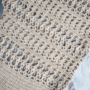 May include: A close-up of a beige crocheted rug with a delicate pattern. The rug is made of natural fibers and has a soft, textured surface.