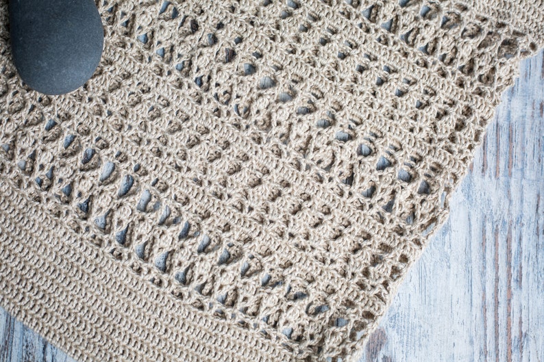 May include: A close-up of a beige crocheted rug with a delicate pattern. The rug is made of natural fibers and has a soft, textured surface.
