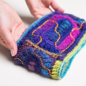 May include: A colorful knitted headband with a blue, green, purple, and pink color scheme. The headband is decorated with gold thread.