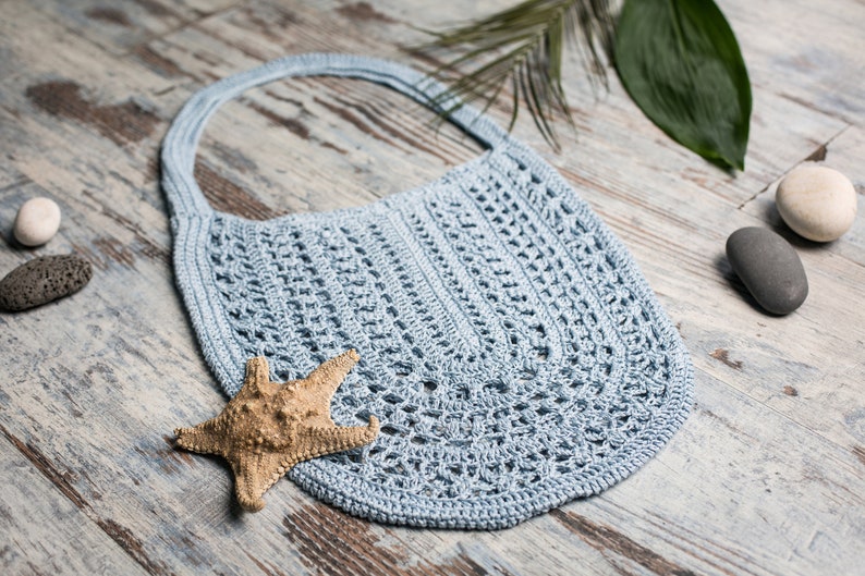 Handmade crochet shoulder bag in soft blue, styled with sea stones and starfish on a light background – Summer Cloud by Kate Kosenko