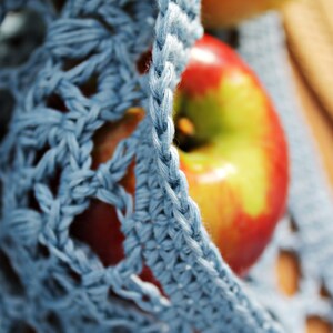 May include: A close-up of a red apple with yellow highlights, partially covered by a blue crocheted fabric.