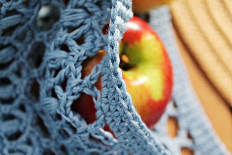 May include: A close-up of a red apple with yellow highlights, partially covered by a blue crocheted fabric.