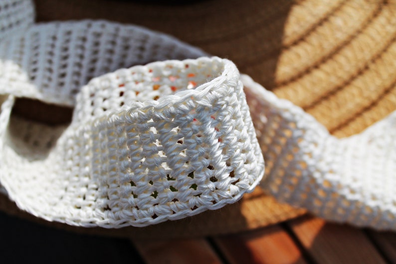 May include: White crocheted trim with a woven texture. The trim is folded and shows the intricate detail of the crocheted stitches.