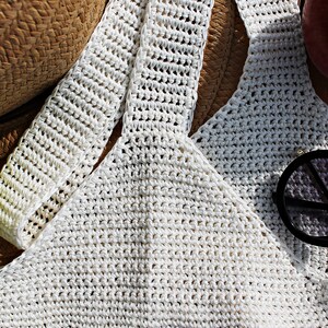 May include: White crochet top with a straw hat and sunglasses. The top is made of a fine, delicate yarn and has a loose, flowing fit. The hat is made of natural straw and has a wide brim. The sunglasses are round and have black frames.