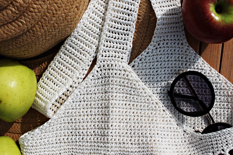 May include: White crochet top with a straw hat and sunglasses. The top is made of a fine, delicate yarn and has a loose, flowing fit. The hat is made of natural straw and has a wide brim. The sunglasses are round and have black frames.