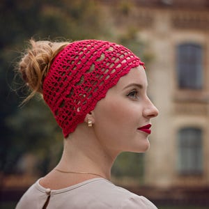 May include: A woman wearing a red crocheted headband. The headband has a delicate, lacy pattern.