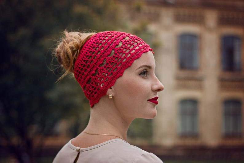 May include: A woman wearing a red crocheted headband. The headband has a delicate, lacy pattern.