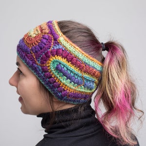 May include: A colorful crocheted headband with a multi-colored pattern. The headband is worn by a person with a ponytail.