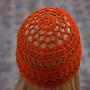 A close-up photo of a crocheted lace hat with an intricate pattern and fingering weight yarn. View from top of the head.