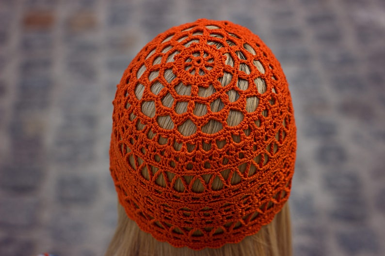 A close-up photo of a crocheted lace hat with an intricate pattern and fingering weight yarn. View from top of the head.