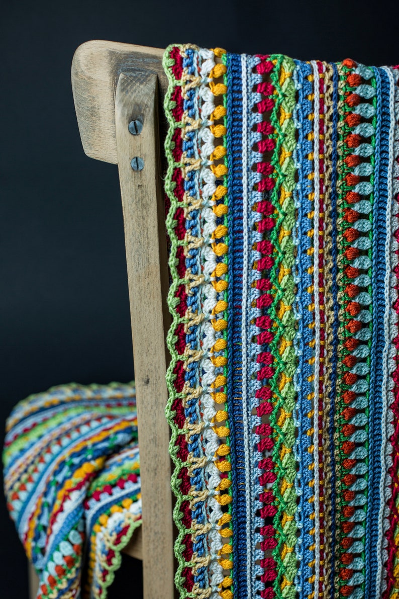 A crocheted, bright, multi-colored scarf with an intricate pattern is hanging on a chair, set against a black background.