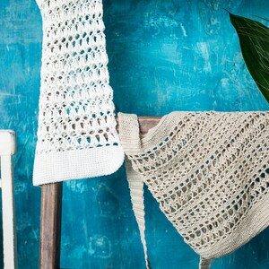 May include: Two crocheted bags hanging on a wooden ladder against a blue wall. The bag on the left is white and the bag on the right is beige.