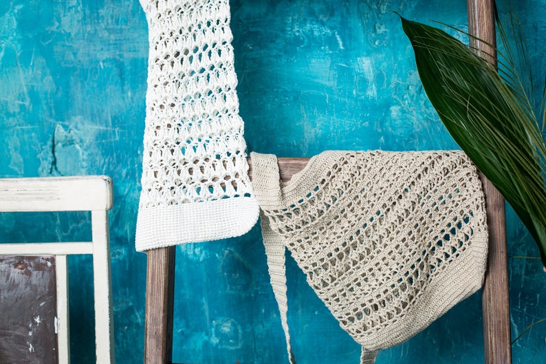 May include: Two crocheted bags hanging on a wooden ladder against a blue wall. The bag on the left is white and the bag on the right is beige.