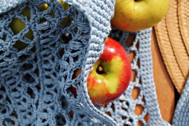 May include: A blue crocheted bag with two apples inside. One apple is red and the other is green.