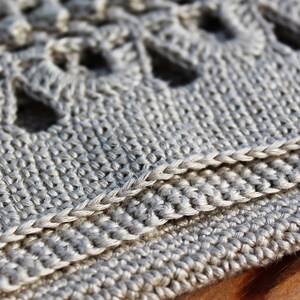 May include: Close-up of a beige crocheted fabric with a textured pattern. The fabric is folded over and the edges are visible.
