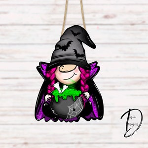 May include: A witch gnome ornament with a black hat, pink hair, and a green cauldron with bones. The gnome is wearing a purple cape with glitter accents.