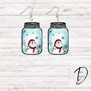May include: A pair of dangle earrings featuring a snowman inside a mason jar with a blue and white background. The snowman is wearing a red hat and scarf.