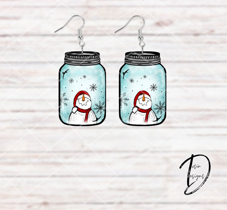 May include: A pair of dangle earrings featuring a snowman inside a mason jar with a blue and white background. The snowman is wearing a red hat and scarf.