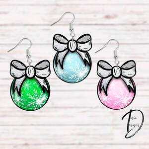 Può includere: Tre paia di orecchini a forma di ornamento natalizio. Ogni paio presenta un fiocco argentato e un ornamento rotondo con un motivo a fiocco di neve bianco. Gli ornamenti sono verde, blu e rosa.