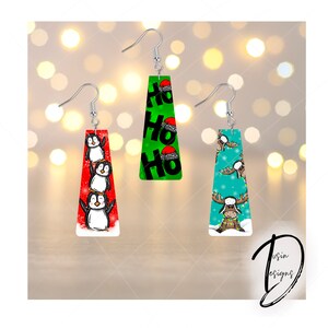 Op de afbeelding: Drie paar kerstoorbellen. Eén paar heeft pinguïns, een ander heeft de tekst "HO HO HO" met kerstmutsen en de derde toont een eland met een hoed en kerstverlichting. Elke oorbel heeft een zilveren haak.