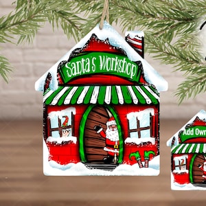May include: A red and white wooden Christmas ornament shaped like a house with a green awning that says "Santa's Workshop". There is a small elf peeking out of a window and Santa Claus is standing in the doorway.