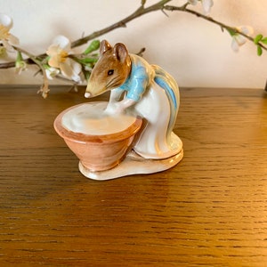 May include: A ceramic figurine of a mouse wearing a blue dress and white apron, churning butter in a brown bowl.