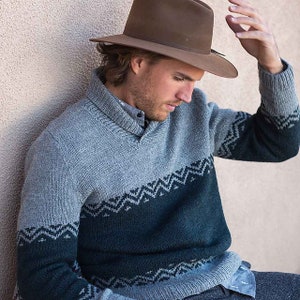 May include: A gray and green patterned sweater with a v-neck collar. The sweater has a brown felt hat on top of it.