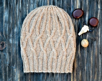 May include: A beige knitted hat with a cable knit pattern. The hat is lying on a dark wood surface.