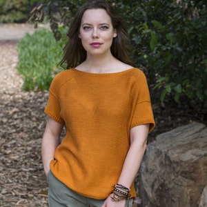 May include: A woman wearing a burnt orange knitted sweater with short sleeves and green pants. She is wearing several bracelets on her wrist.