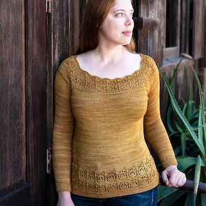 Könnte beinhalten: Eine Frau trägt einen langärmeligen, senfgelben Pullover mit einem zarten Spitzenmuster am Ausschnitt und Saum. Sie steht neben einer Holztür und einer großen grünen Pflanze.