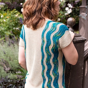 May include: A beige knitted top with teal and green wavy stripes down the back. The top has short sleeves and a scoop neck.