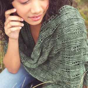 Könnte beinhalten: Ein grüner gestrickter Schal mit einem Spitzenmuster. Der Schal ist über die Schultern einer Person gelegt.