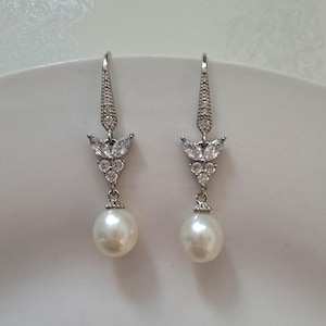 May include: A pair of silver dangle earrings with a pearl drop and a crystal flower design.