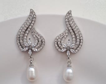 May include: A pair of silver dangle earrings with a pearl drop. The earrings feature a floral design with clear cubic zirconia stones.