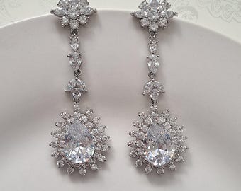 May include: A pair of silver dangle earrings with large pear-shaped clear cubic zirconia stones surrounded by smaller stones. The earrings have a floral design at the top.
