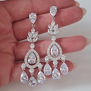 Peut inclure: Boucles d'oreilles pendantes argentées avec des cristaux transparents étincelants. Elles présentent un design en forme de goutte d'eau avec plusieurs pendentifs en cristal. Les boucles d'oreilles ont un motif en forme de feuille et sont parfaites pour les occasions spéciales.