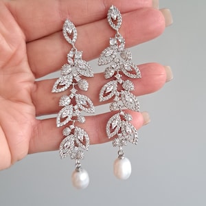 May include: Silver dangle earrings with a pearl drop and a design of cascading leaves encrusted with clear rhinestones.