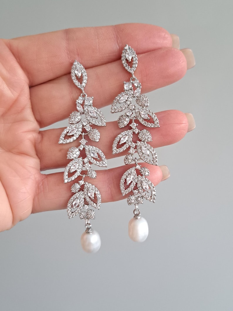 May include: Silver dangle earrings with a pearl drop and a design of cascading leaves encrusted with clear rhinestones.