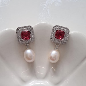 May include: Silver earrings with a red square gemstone and a white pearl drop.