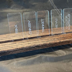 May include: A wooden stand with six clear acrylic cards. The cards have the names "MAX", "CHASSY", "TRINKET", "HEY-YU", "DOCTOR", and "ANTIKUS" written on them.