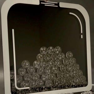 May include: A black and white acrylic coin bank with a white border. The bank is filled with clear acrylic coins etched with a mouse design. A hand is adding a coin to the bank. A pile of coins is at the bottom.
