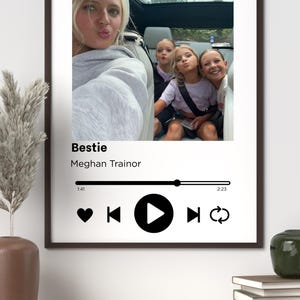 Könnte beinhalten: Gerahmter Druck mit einem Foto von vier Personen in einem Auto. Der Druck enthält den Songtitel "Bestie" von Meghan Trainor sowie eine Musikplayer-Grafik mit Wiedergabe-, Pausen- und Überspringen-Steuerelementen.