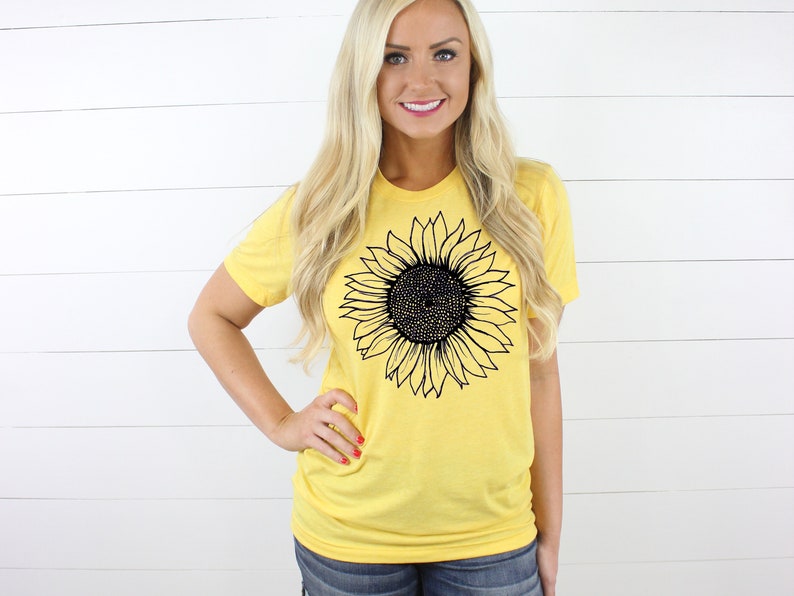 Puede incluir: Una camiseta amarilla con un gr&aacute;fico de girasol en blanco y negro.