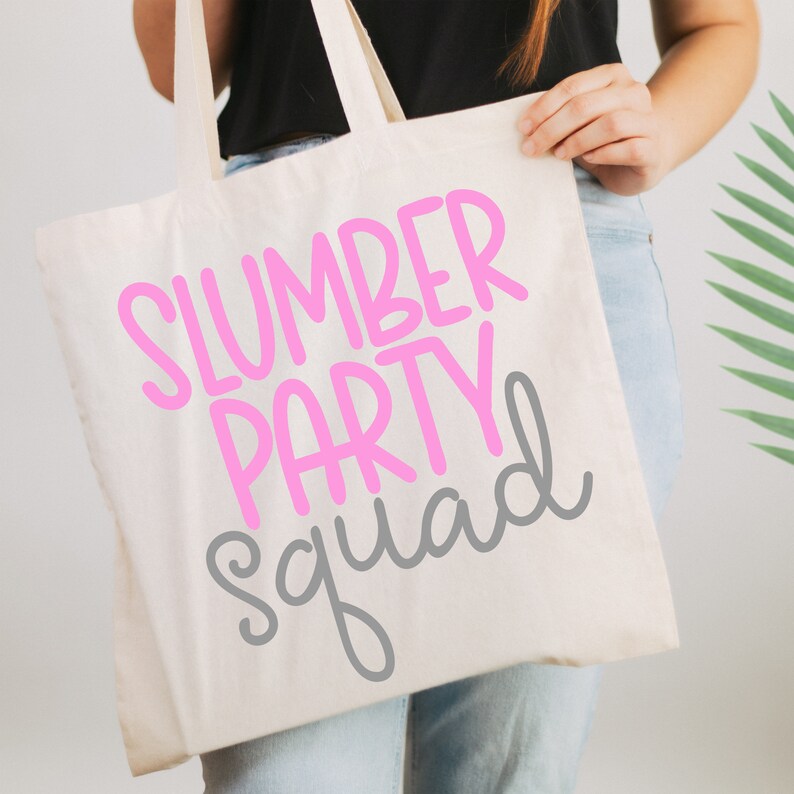 Może przedstawiać: Biała torba z pł&oacute;tna z napisem "Slumber Party Squad" w r&oacute;żowych i szarych literach.
